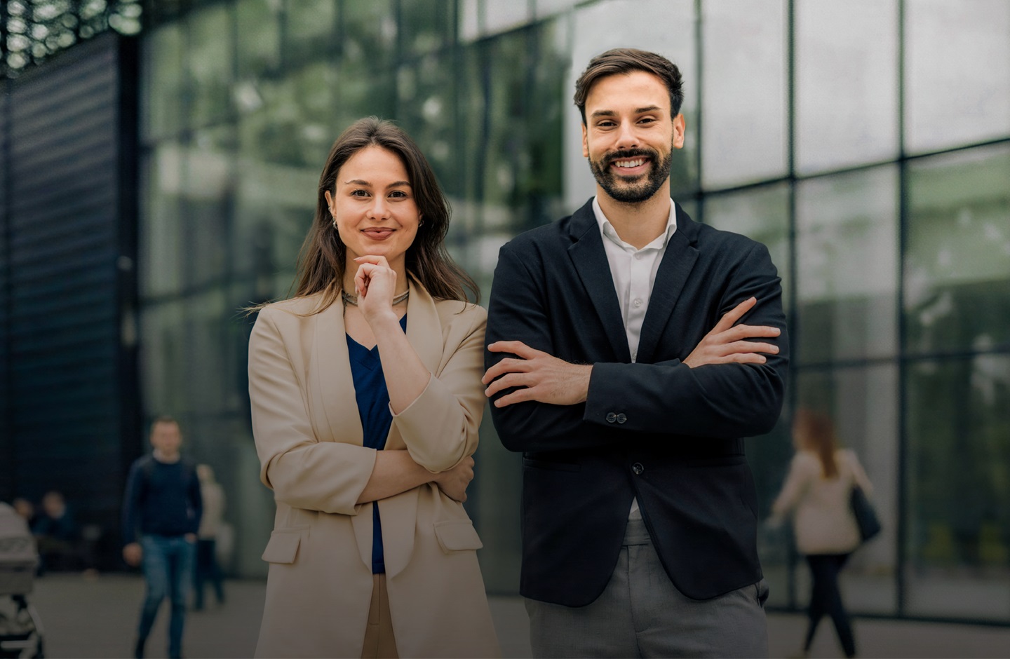 Eine Frau und ein Mann in Business Outfits stehen nebeneinander und blicken selbstbewusst in die Kamera.